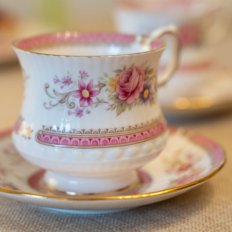 Vista frontal de un dúo de té de porcelana inglesa fina Queen's "Richmond" con cuerpo acanalado, bordes de oro, franja rosa y diseño central de rosas.