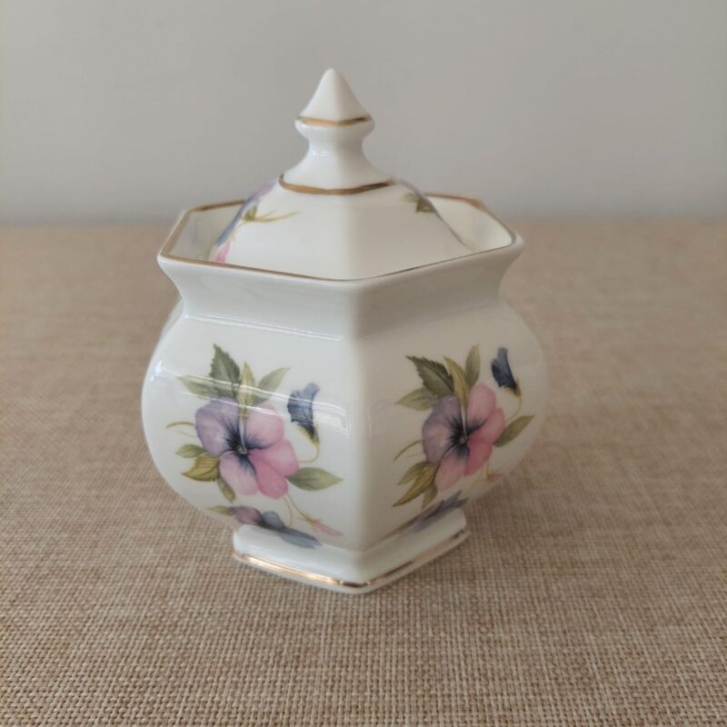 Vista frontal de un azucarero octogonal con tapa de porcelana inglesa Classique China by Modus, decorado con ramilletes de pensamientos en tonos violeta y rosa con bordes perfilados en oro.