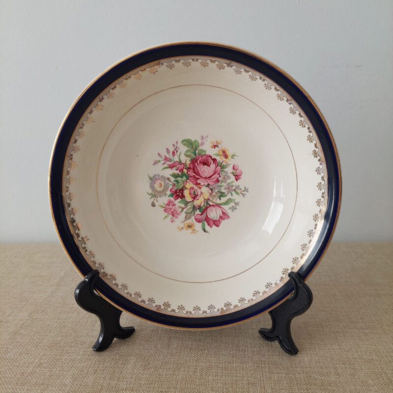 Vista superior de una fuente ensaladera vintage de loza inglesa Washington Pottery con un borde azul cobalto, guirnaldas doradas y un ramo de rosas central.