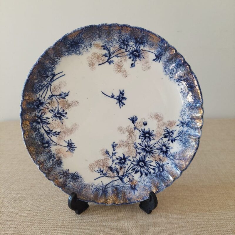 Primer plano del borde festoneado de un plato antiguo de loza inglesa Devon de S. Fielding & Co., mostrando el detalle de las flores azules transferware y el delicado estarcido de oro difuminado.