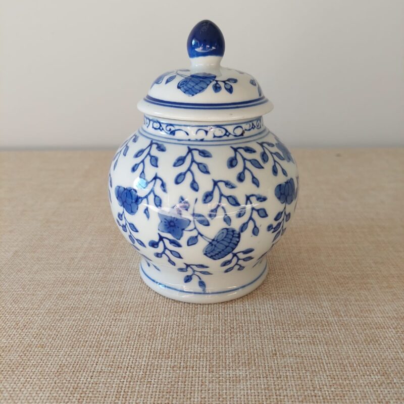 Vista frontal de un potiche miniatura de porcelana blanca bulbosa con tapa, decorado con patrones de flores y hojas en azul cobalto de estilo oriental.