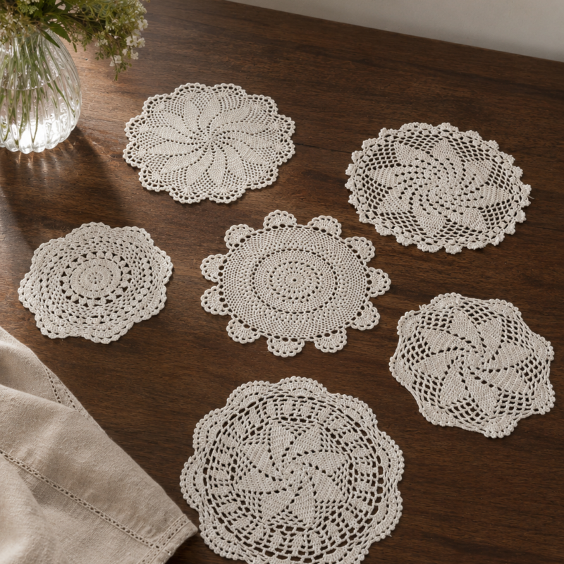 Vista de detalle de 6 tapetes circulares de encaje blanco tejidos a mano a crochet con diferentes patrones geométricos calados, presentados en hilera sobre una superficie de madera oscura.