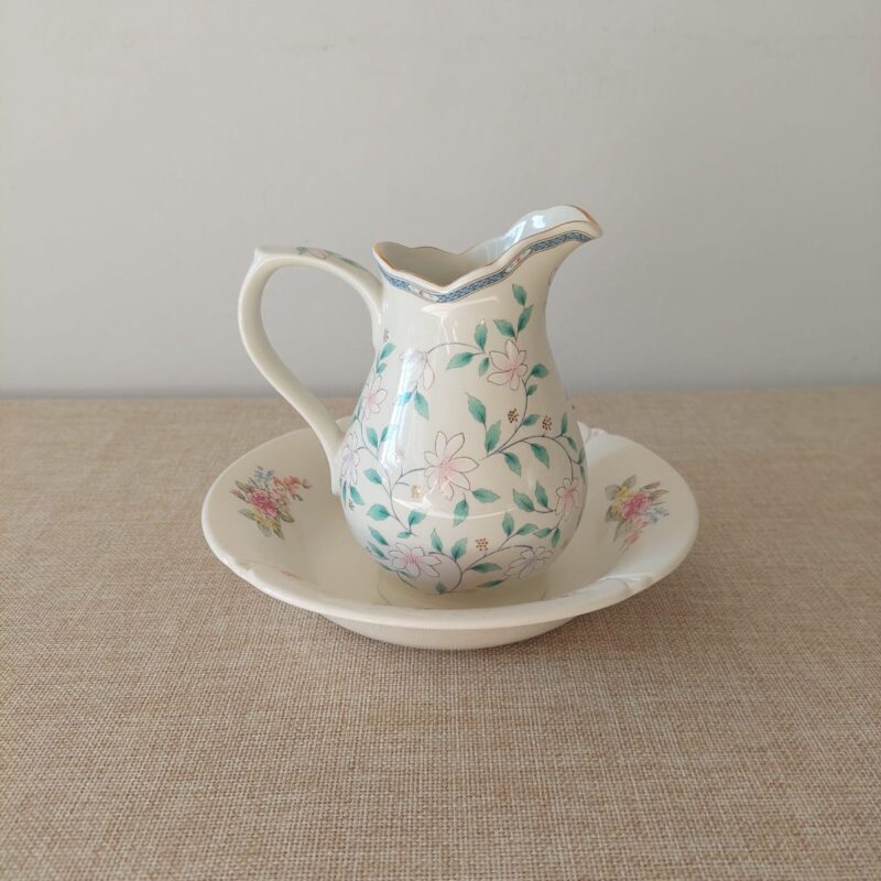 Set de jofaina decorativa vintage compuesto por una jarra de porcelana fina blanca con flores rosadas montada sobre un plato hondo crema de loza inglesa de Staffordshire.