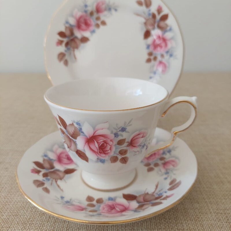 Trío de té de porcelana fina inglesa Queen Anne con diseño de rosas rosadas, flores azules y ribete dorado festoneado.