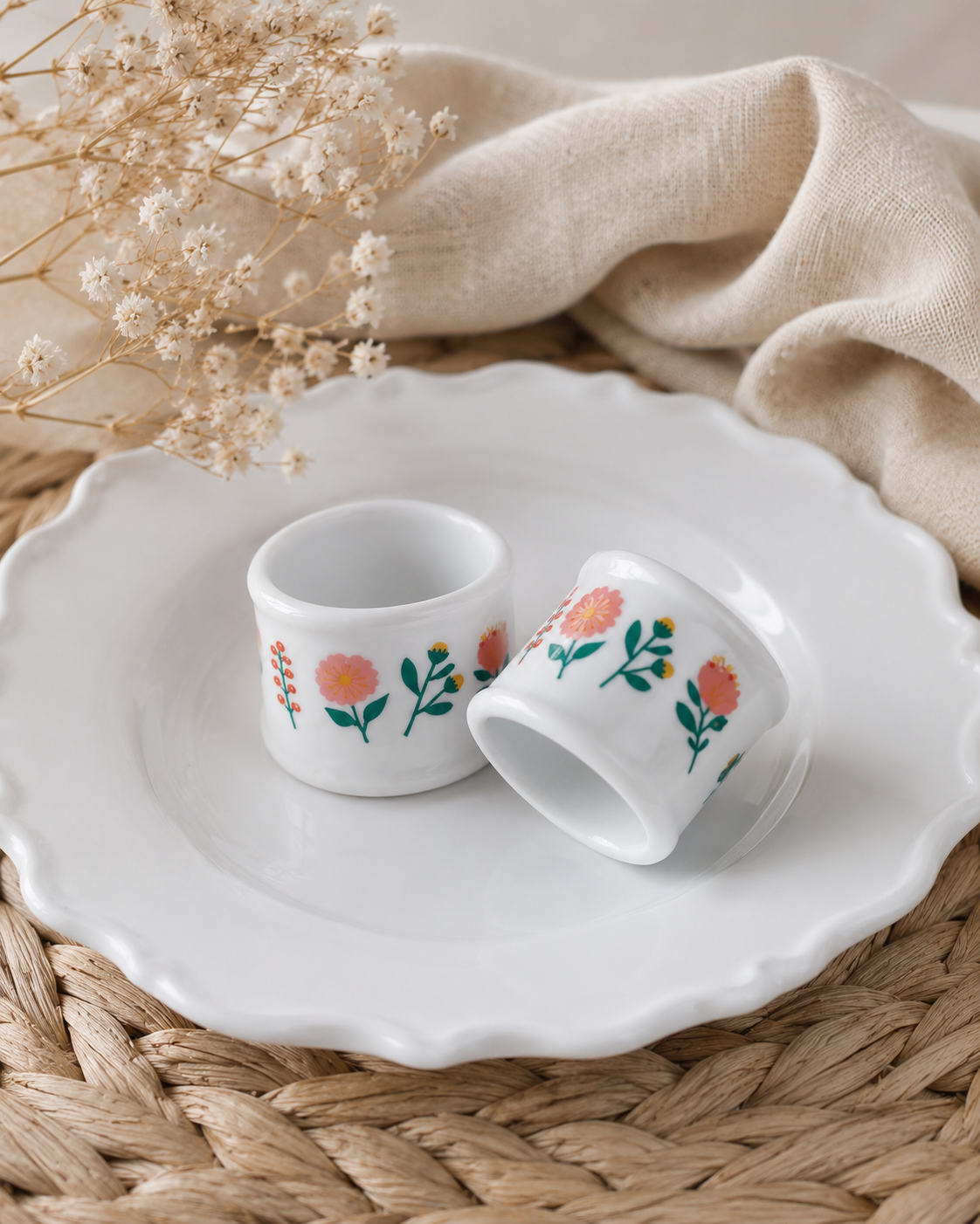 Set de dos anillos para servilleta de porcelana blanca decorados con flores rosadas y hojas verdes, ideales para mesas delicadas y ocasiones especiales.