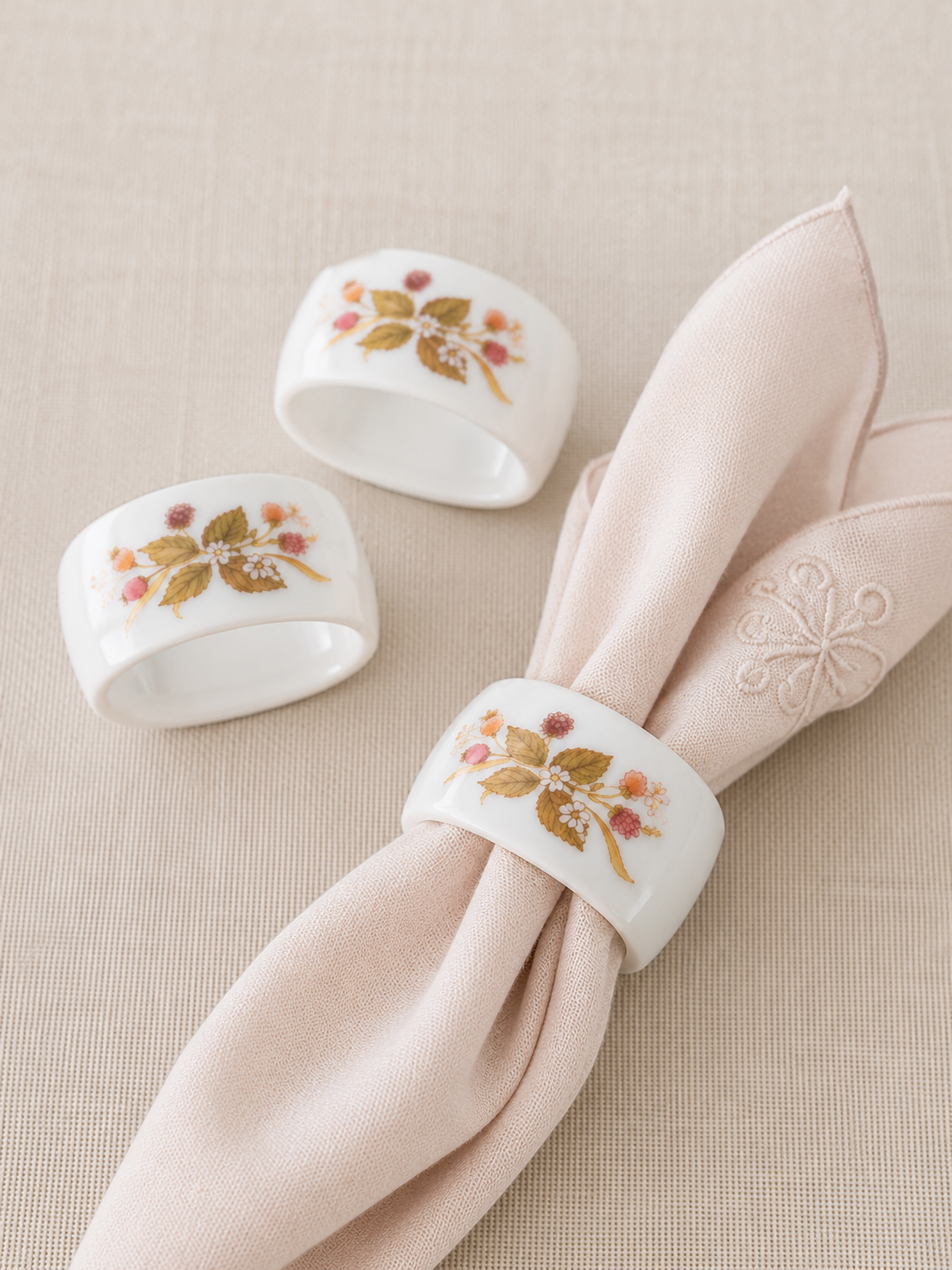Set de tres anillos para servilleta de porcelana blanca con decoración floral silvestre en tonos tierra y rosados, ideales para mesas elegantes y decoraciones de estilo clásico o campestre.