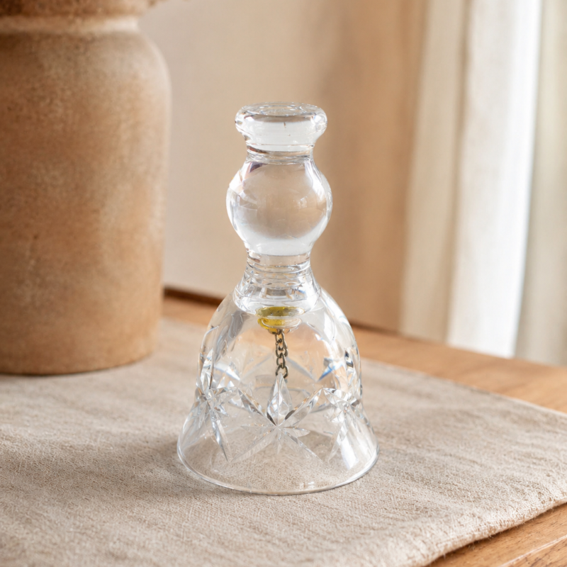 Pequeña campana decorativa de cristal transparente con tallado en forma de estrella y detalle metálico interior.