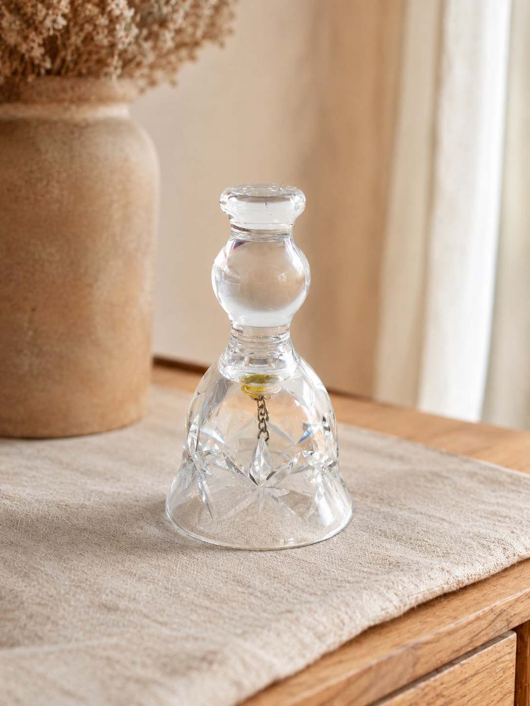 Pequeña campana decorativa de cristal transparente con tallado en forma de estrella y detalle metálico interior.