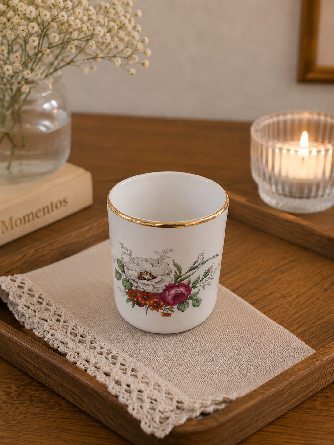 Vista frontal en ángulo de un mini pocillo cilíndrico de cerámica fina inglesa de la marca Braunton Studio Ceramics sobre un fondo beige. Pocillo blanco de 5 cm de alto muestra un delicado ramo de flores silvestres amarillas, rojas y moradas en el centro y un borde superior cubierto por un fino y brillante hilo dorado.