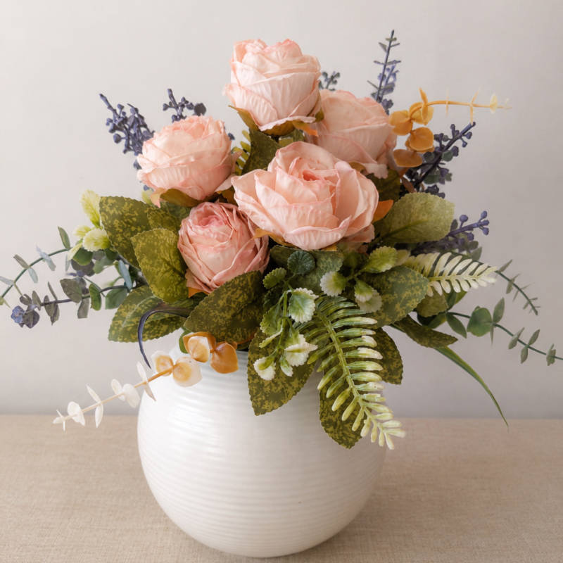 Arreglo floral permanente en tonos rosa empolvado y verde suave dispuesto en florero de cerámica blanca, ideal para decorar espacios acogedores y elegantes.