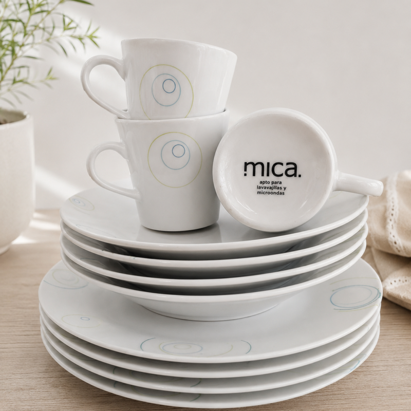 Set de vajilla Mica compuesto por platos llanos, platos hondos y tazas de cerámica blanca con diseño circular en tonos azul y verde suave.