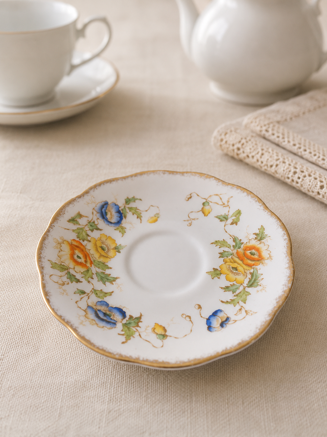 Plato de té Royal Albert Crown China de porcelana inglesa con borde festoneado dorado y delicado diseño floral en tonos azul, amarillo y naranja.