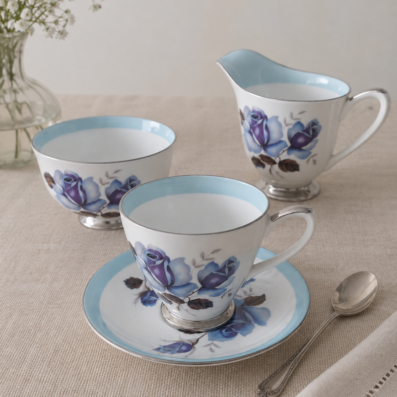 Colección vintage Windsor Bone China Made in England con dúo de té, lechero y terronero decorados con rosas azules, borde celeste y terminaciones plateadas.